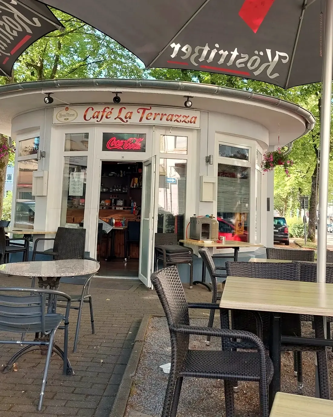 Unser runder weißer Pavillon mit dem roten Schriftzug, davor Tische und Stühle unter Sonnenschirmen und Bäumen