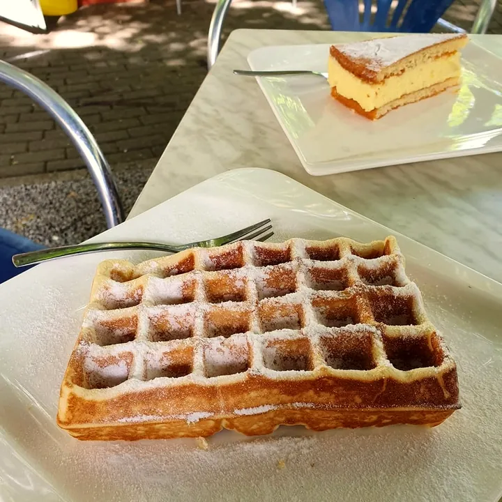 Waffel mit Puderzucker und ein Stück Torte auf einem Marmortisch draußen